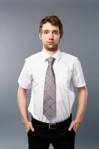 Serious businessman posing with hands in pockets on grey background — Stock Photo