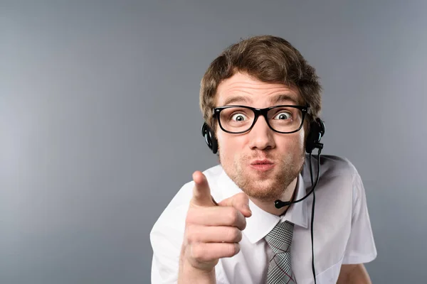 Operador de centro de llamadas enojado en auriculares y gafas apuntando con el dedo a la cámara - foto de stock