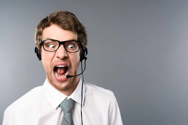 Irritated call center operator in headset and glasses yelling on grey background — Stock Photo