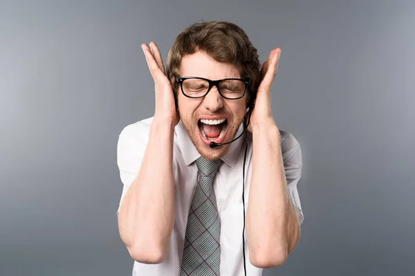 Operador de centro de llamadas enojado en auriculares y gafas gritando con las manos en las orejas — Stock Photo