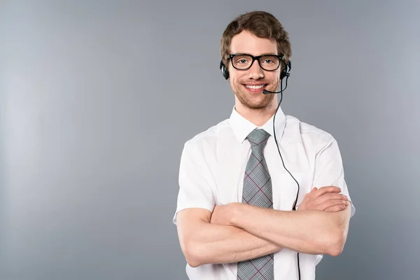 Opérateur de centre d'appels souriant en lunettes et casque avec bras croisés sur fond gris — Photo de stock