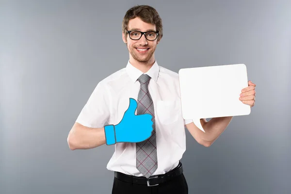 Positive businessman in glasses with paper cut thumb up holding white empty card on grey background — Stock Photo