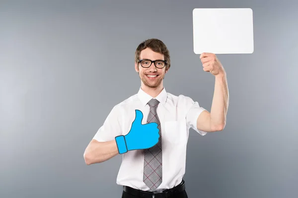 Hombre de negocios feliz en vasos con el pulgar cortado de papel hacia arriba sosteniendo la tarjeta vacía blanca sobre fondo gris - foto de stock