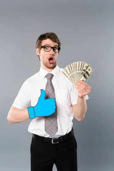 Sorprendido hombre de negocios en gafas con el pulgar cortado de papel hacia arriba la celebración de billetes de dólar sobre fondo gris - foto de stock