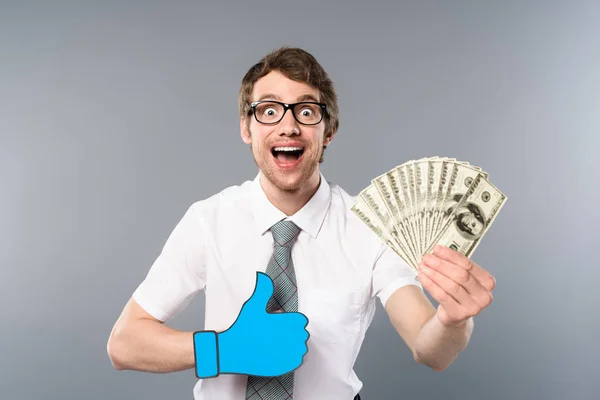 Hombre de negocios feliz en gafas con papel cortado pulgar hacia arriba la celebración de billetes de dólar sobre fondo gris - foto de stock