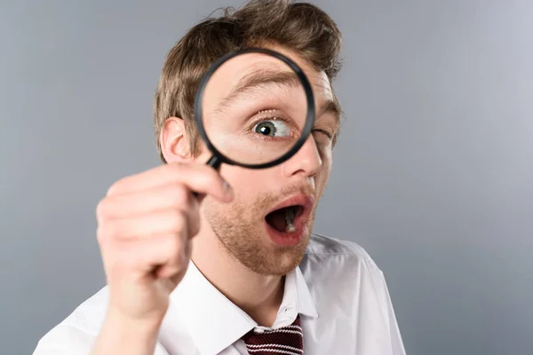 Shocked businessman with funny face expression looking in magnifier on grey background — Stock Photo