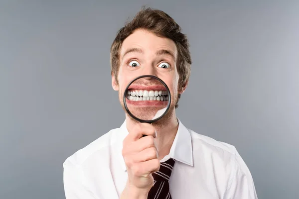 Homme d'affaires souriant avec expression drôle visage tenant loupe sur fond gris — Photo de stock