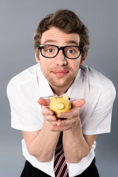 Guapo hombre de negocios en gafas sosteniendo alcancía sobre fondo gris - foto de stock