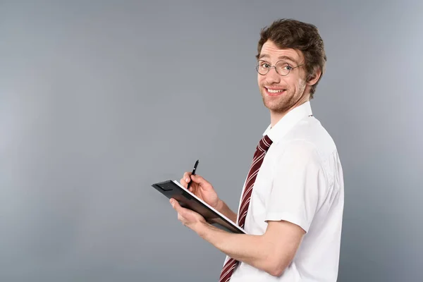 Улыбающийся бизнесмен с ручкой на бумаге на сером фоне — стоковое фото