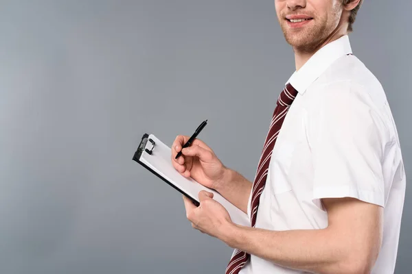 Abgeschnittene Ansicht eines lächelnden Geschäftsmannes mit Federschrift auf Klemmbrett auf grauem Hintergrund — Stockfoto