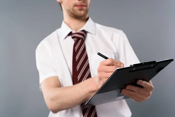 Vue recadrée de l'homme d'affaires avec stylo écriture sur presse-papiers sur fond gris — Photo de stock