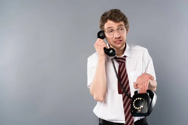 Confused businessman in glasses talking on vintage phone on grey — Stock Photo