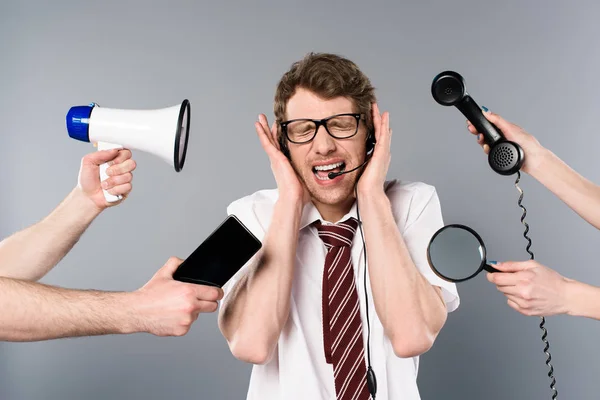 Stressed call center operator in headset screaming near megaphone, smartphone, magnifier and telephone — Stock Photo