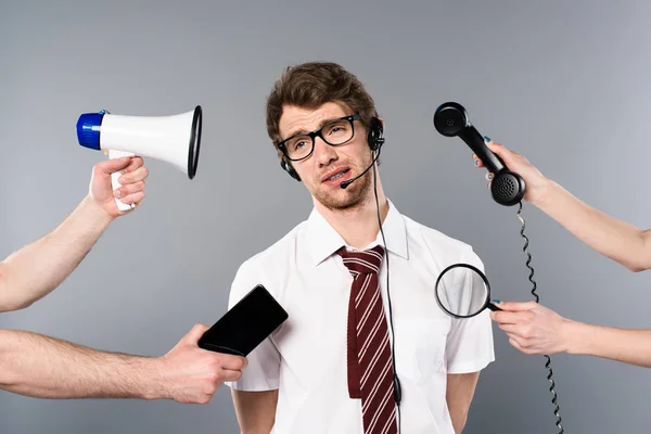 Exhausted call center operator in headset near megaphone, smartphone, magnifier and telephone — Stock Photo