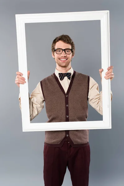 Homme souriant tenant cadre blanc sur fond gris — Photo de stock