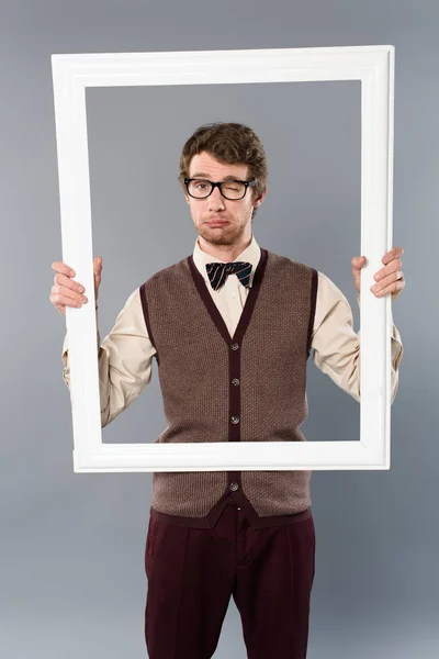Homme en lunettes clin d'oeil et tenant cadre blanc sur fond gris — Photo de stock