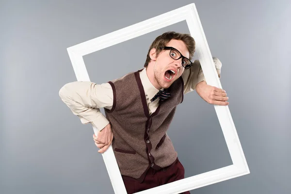Gracioso hombre gritando y sosteniendo marco blanco sobre fondo gris - foto de stock