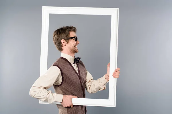 Vue latérale d'un homme souriant tenant un cadre blanc sur fond gris — Photo de stock