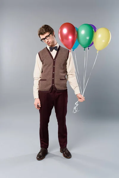 Sad man in glasses holding multicolored balloons on grey background — Stock Photo