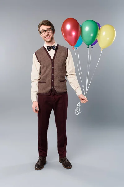 Smiling man in glasses holding multicolored balloons on grey background — Stock Photo