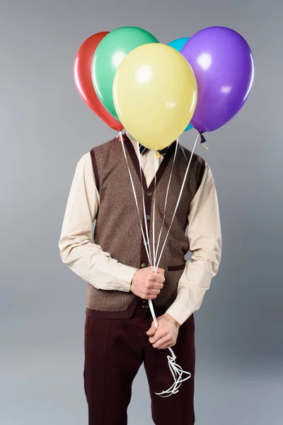 Hombre con cara oscura sosteniendo globos multicolores sobre fondo gris - foto de stock