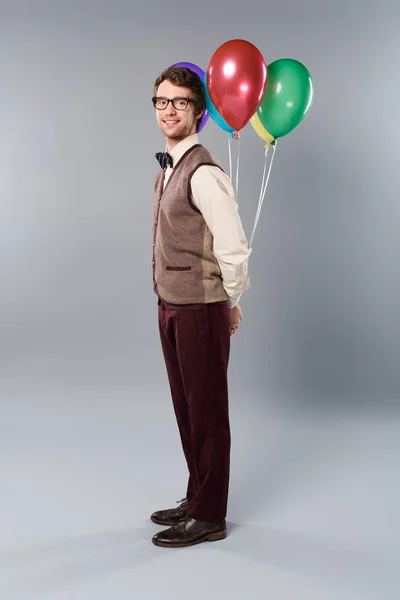 Позитивний чоловік в окулярах тримає різнокольорові кульки на сірому фоні — стокове фото