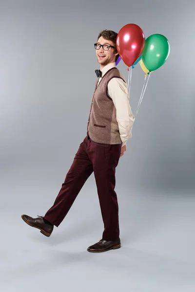 Gracioso hombre en gafas sosteniendo globos multicolores sobre fondo gris - foto de stock