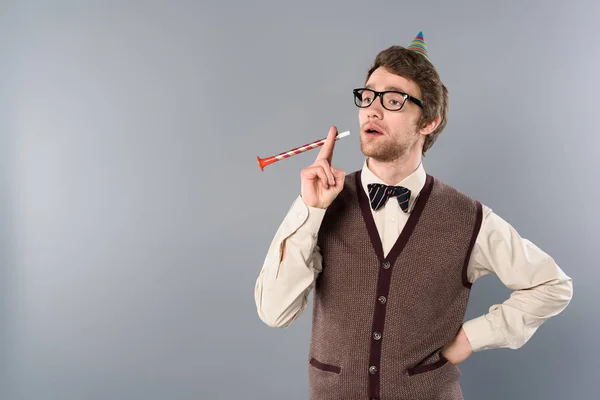 Homme drôle dans des lunettes et casquette de fête imitant la corne de fête fumeur sur fond gris — Photo de stock