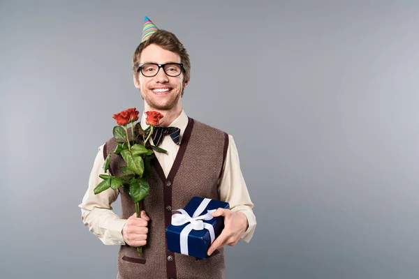 Smiling man in party cap holding bouquet of roses and gift box — Stock Photo