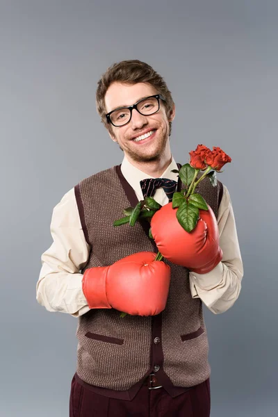 Hombre feliz en gafas y guantes de boxeo sosteniendo ramo de rosas sobre fondo gris - foto de stock