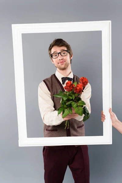 Homme dans un cadre blanc tenant bouquet de roses sur fond gris — Photo de stock