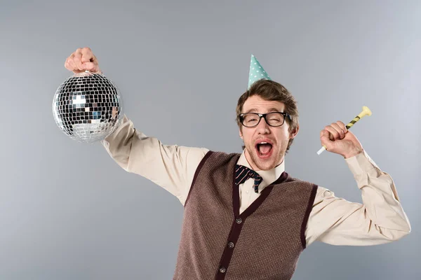 Excited man in party cap holding shiny disco ball and party horn on grey background — Stock Photo