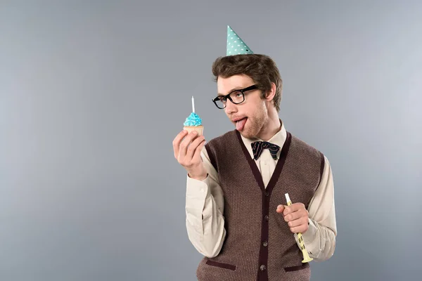 Homem em óculos e tampão de festa com expressão facial engraçada segurando cupcake e chifre de festa — Fotografia de Stock