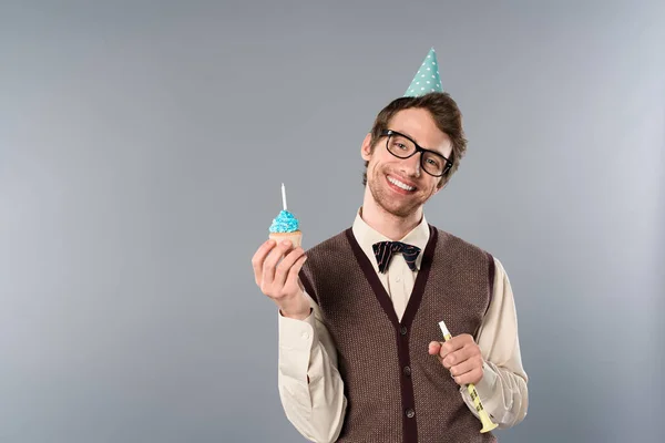 Sonriente hombre en gafas y partido gorra celebración cupcake con vela - foto de stock