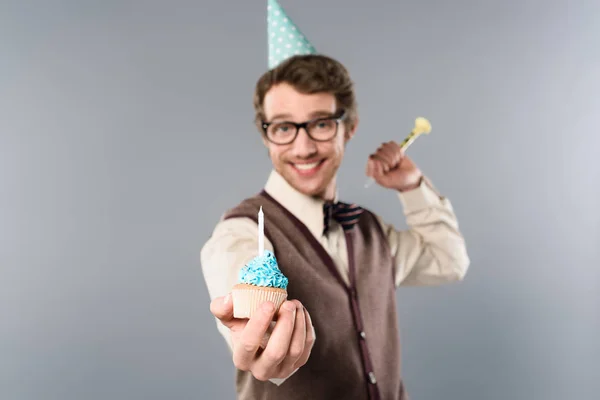 Селективное внимание улыбающегося мужчины в очках и кепке для вечеринок, держащего кекс со свечой — стоковое фото
