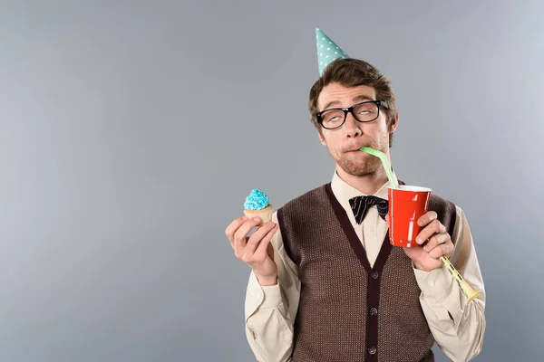 Man in glasses and party cap with funny face expression holding cupcake and drinking soda — Stock Photo