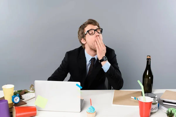 Geschäftsmann gähnt am Arbeitsplatz in der Nähe von Cupcake und Pappbechern isoliert auf grau — Stockfoto