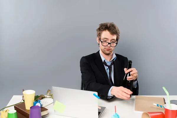 Drunk businessman sitting at workplace with bottle of champagne isolated on grey — Stock Photo