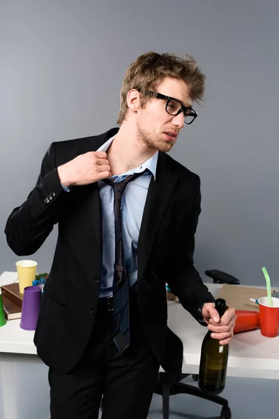 Drunk businessman in glasses standing near workplace with bottle of champagne — Stock Photo