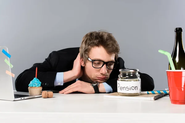 Triste uomo d'affari in occhiali guardando moneybox pensione isolato su grigio — Foto stock