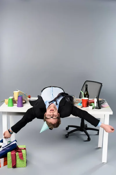 Бізнесмен в партійній шапці і окулярах спить на столі на безладному робочому місці — стокове фото