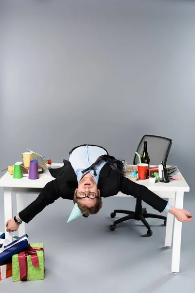 Businessman in party cap and glasses sleeping on table at messy workplace — Stock Photo