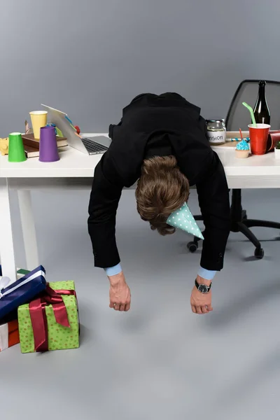 Hombre de negocios con gorra de fiesta durmiendo en la mesa en el lugar de trabajo desordenado - foto de stock