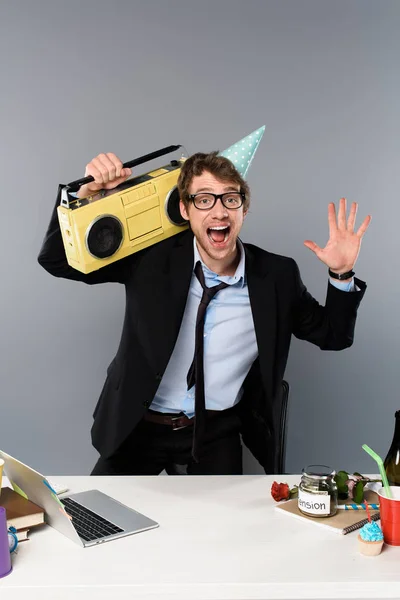 Hombre de negocios feliz en el lugar de trabajo en la tapa del partido con grabadora de cinta vintage sobre fondo gris - foto de stock