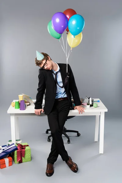 Drunk businessman in party cap sleeping at messy festive workplace — Stock Photo
