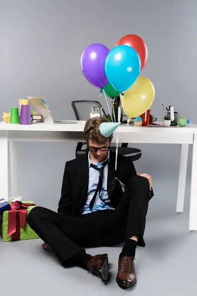 Borracho hombre de negocios en partido gorra durmiendo en desordenado festivo decorado lugar de trabajo - foto de stock