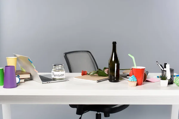 Lieu de travail désordonné avec bouteille de champagne, gobelets en papier, tirelire et ordinateur portable sur table blanche — Photo de stock