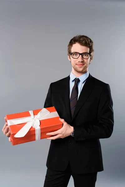 Lächelnder Geschäftsmann mit Geschenk auf grauem Hintergrund — Stockfoto