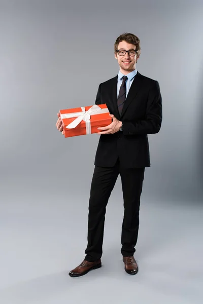 Happy businessman holding present on grey background — Stock Photo