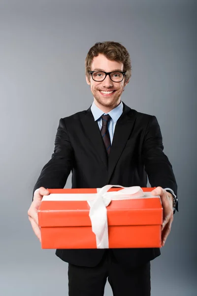 Счастливый бизнесмен держит оранжевый подарок на сером фоне — стоковое фото